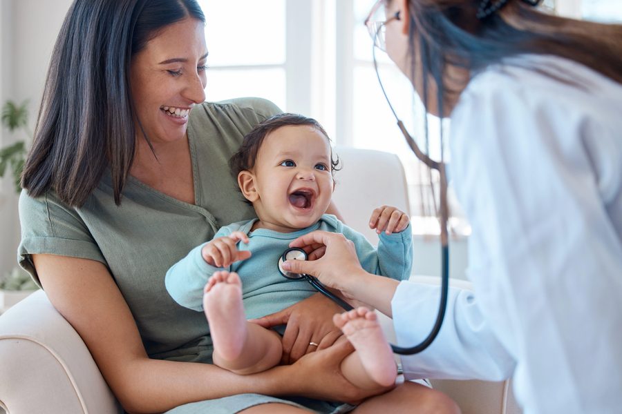 A paediatrician listening to a happy baby's heartbeat with a stethoscope while the mother looks on